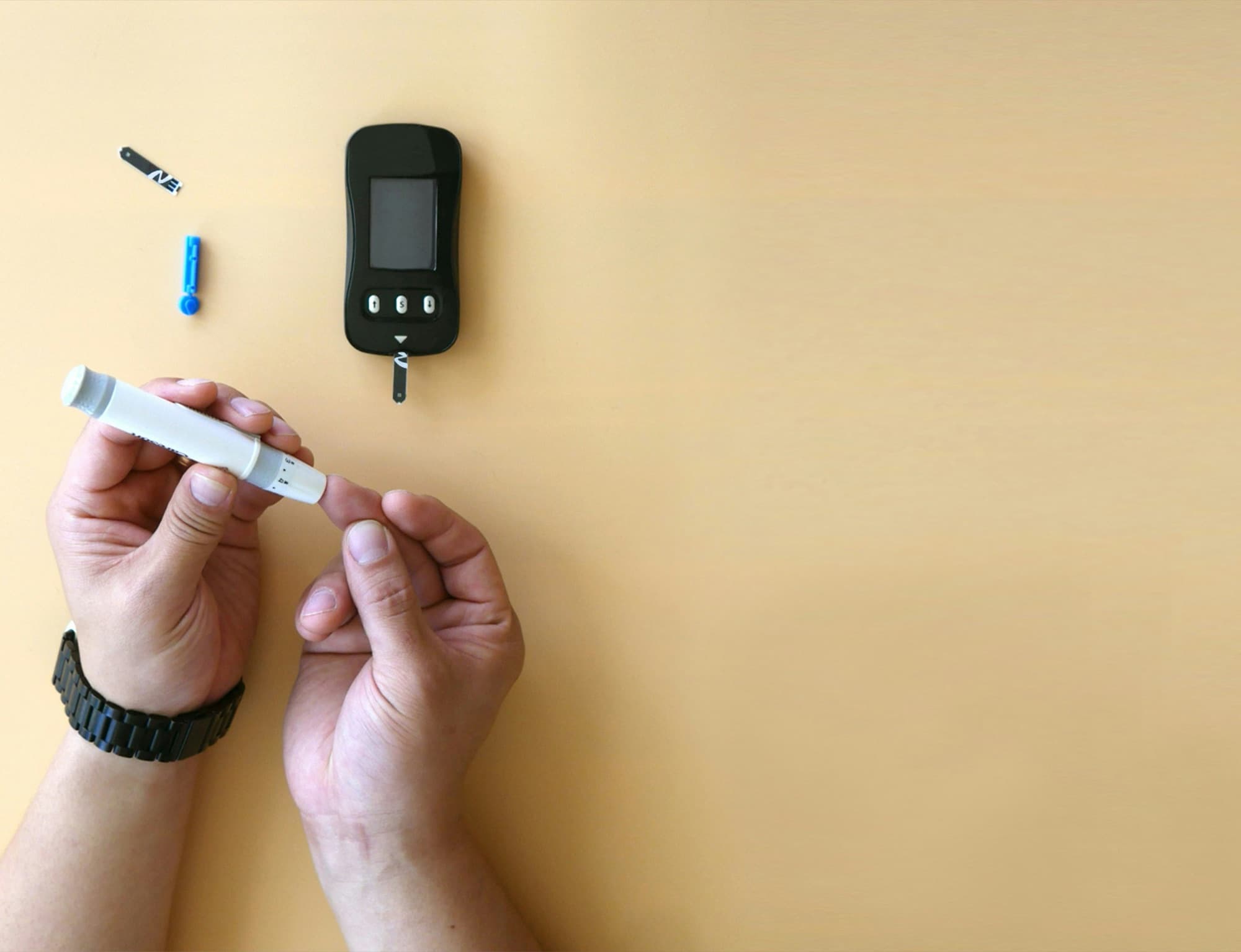 A person doing a finger-stick blood glucose test next to a glucometer