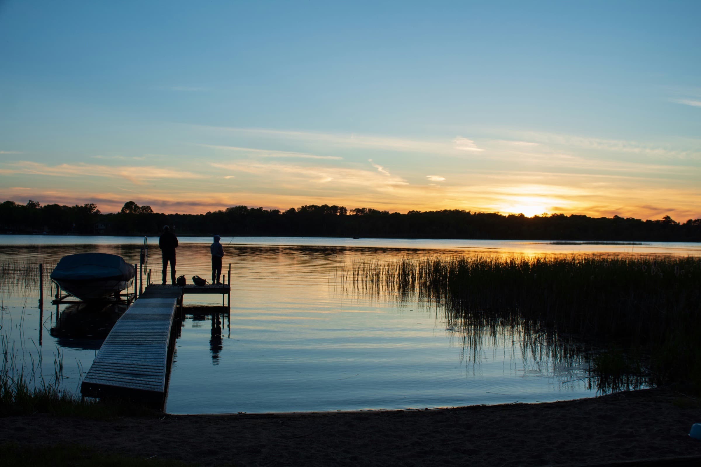 Sunset over a Minnesota lake with two people fishing from a dock